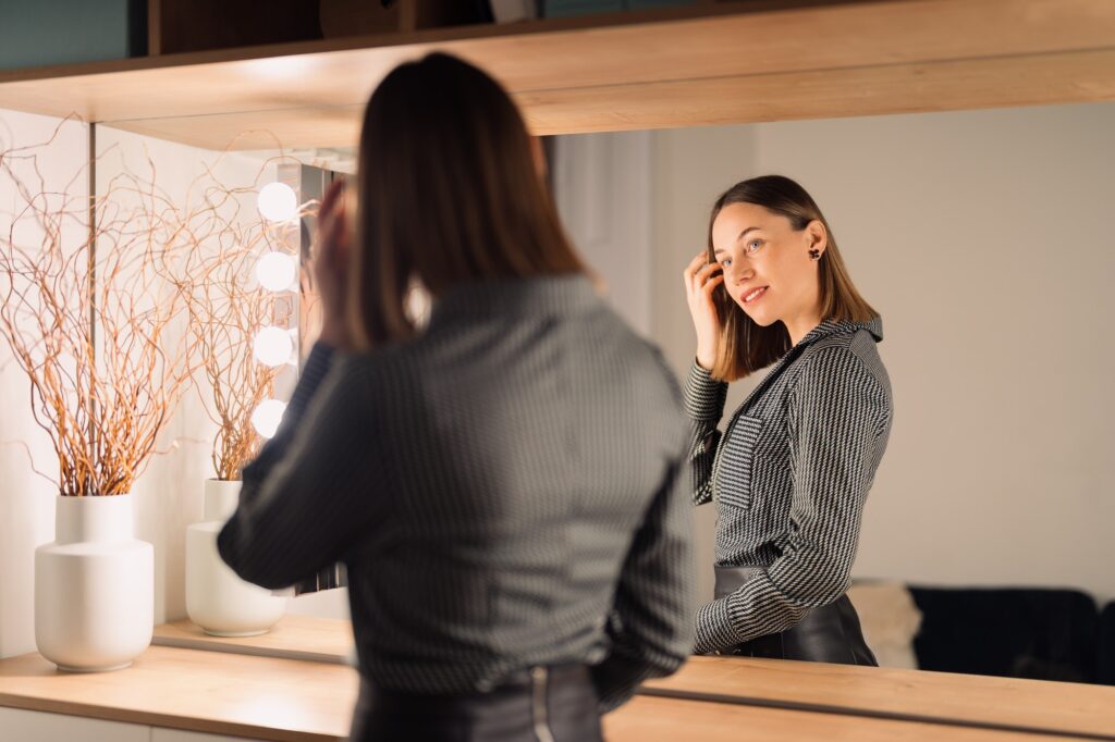 Confident woman looking to her reflection into the mirror