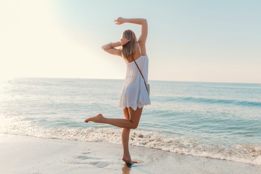 young attractive happy woman dancing turning around by sea beach in white dress vacation